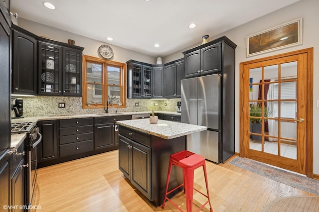 kitchen featuring stainless steel appliances, backsplash, glass insert cabinets, a sink, and light wood-type flooring