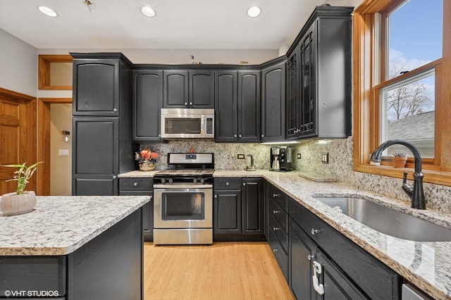 kitchen with light wood finished floors, tasteful backsplash, appliances with stainless steel finishes, and a sink