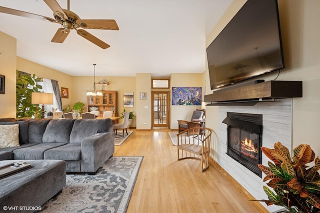 living area with light wood-style flooring, a tiled fireplace, and ceiling fan with notable chandelier