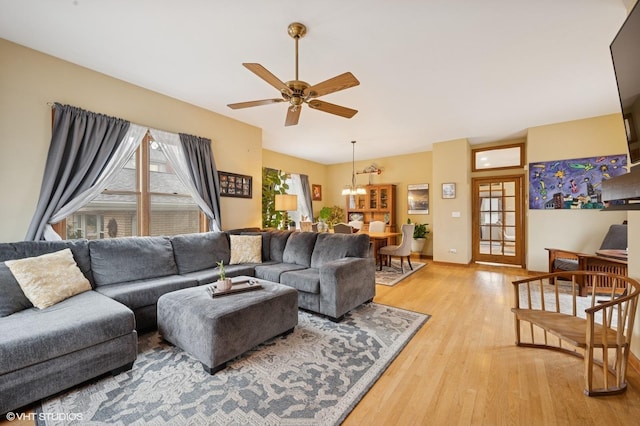 living area with baseboards, light wood finished floors, and ceiling fan with notable chandelier