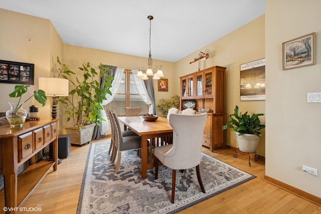 dining space with baseboards, light wood finished floors, and an inviting chandelier