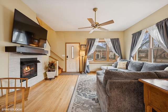 living room featuring stairway, a fireplace, light wood-style flooring, and a ceiling fan