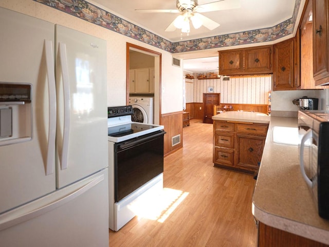 kitchen with wallpapered walls, washer / clothes dryer, white appliances, brown cabinetry, and wainscoting