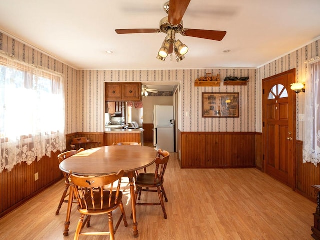 dining room with wainscoting, wallpapered walls, light wood-style floors, and ceiling fan