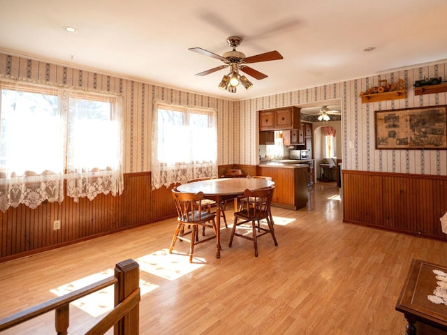 dining space featuring a wainscoted wall, light wood-style flooring, arched walkways, wallpapered walls, and ceiling fan