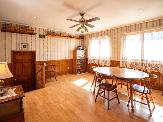 dining area featuring visible vents, a ceiling fan, wallpapered walls, wainscoting, and light wood finished floors