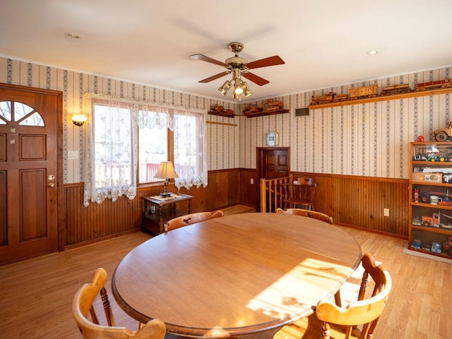 dining area featuring wallpapered walls, ceiling fan, light wood-type flooring, and wainscoting