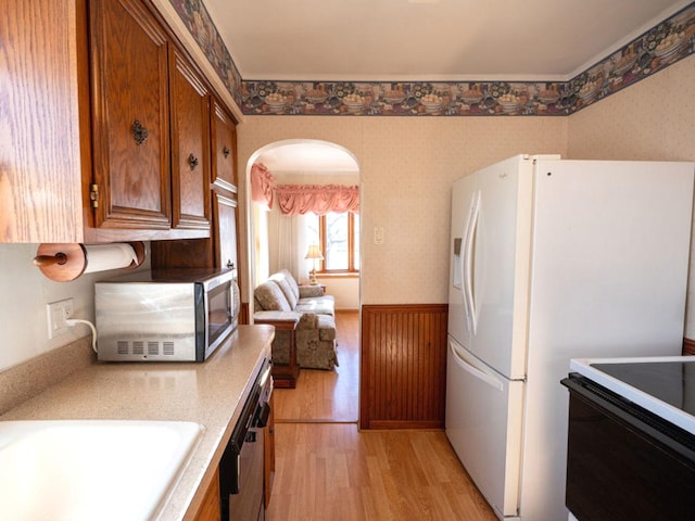 kitchen featuring stainless steel microwave, arched walkways, wainscoting, and wallpapered walls