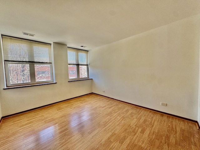 empty room with wood finished floors, visible vents, and baseboards