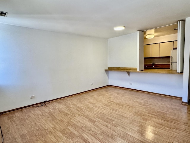 empty room featuring a sink, wood finished floors, visible vents, and baseboards