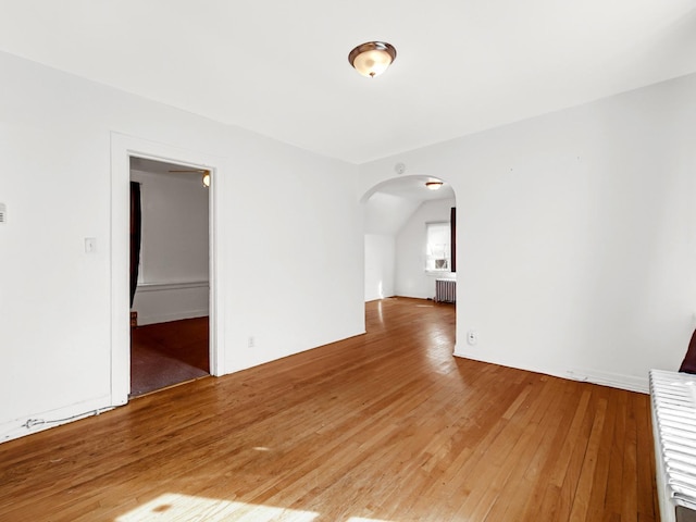 empty room featuring arched walkways, radiator, and light wood-style flooring