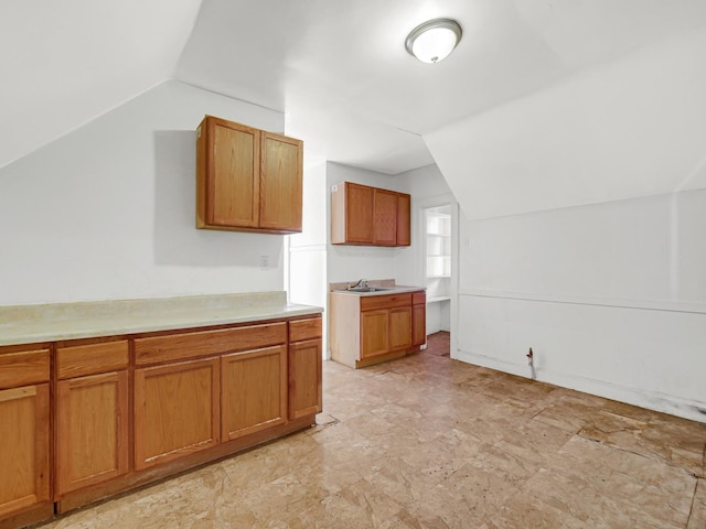 kitchen featuring brown cabinetry, vaulted ceiling, light countertops, and a sink