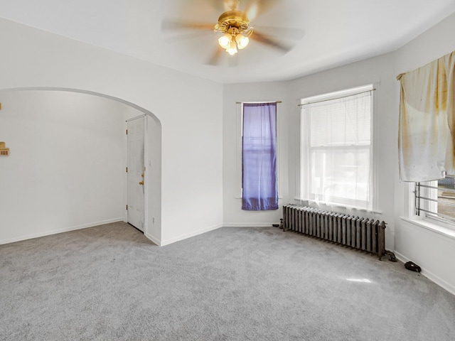 carpeted spare room with radiator, a healthy amount of sunlight, arched walkways, and ceiling fan