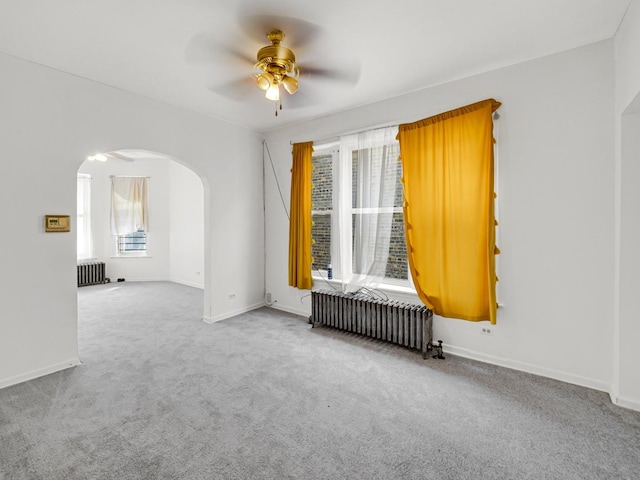 unfurnished room with radiator heating unit, arched walkways, carpet floors, and ceiling fan