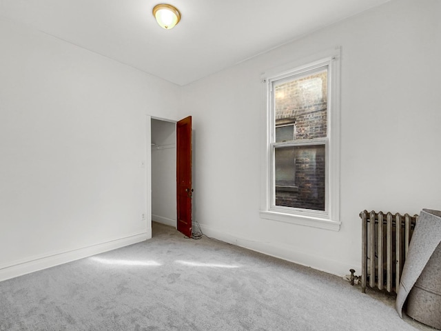 empty room featuring carpet flooring, radiator, and baseboards