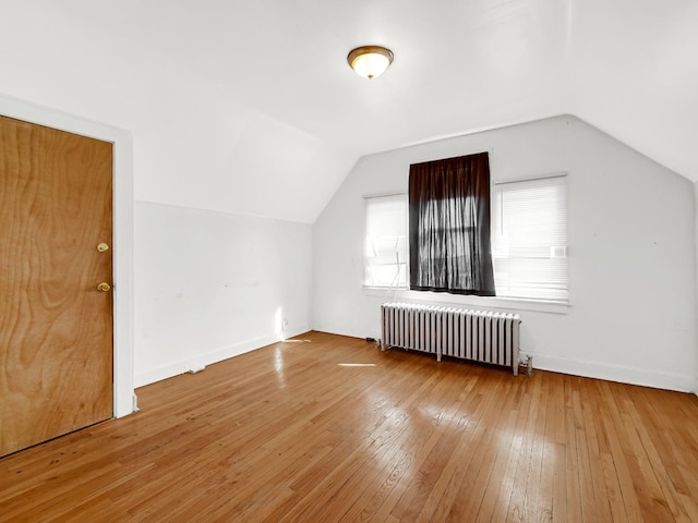 additional living space featuring baseboards, lofted ceiling, radiator heating unit, and hardwood / wood-style flooring