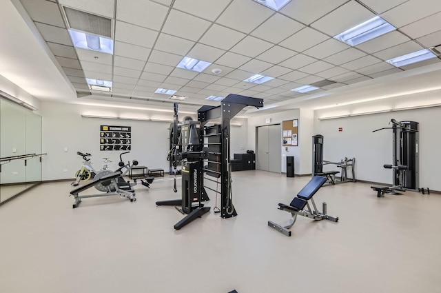 gym with a paneled ceiling and baseboards