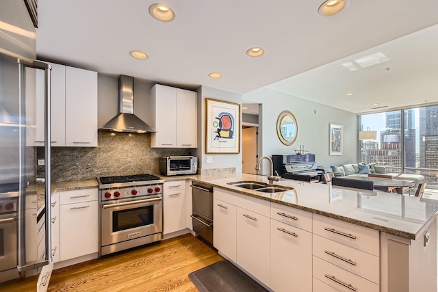 kitchen featuring luxury range, decorative backsplash, a sink, a peninsula, and wall chimney exhaust hood