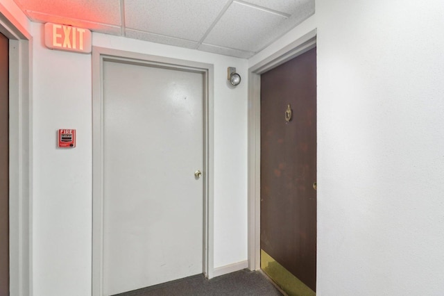 corridor featuring a paneled ceiling and dark carpet