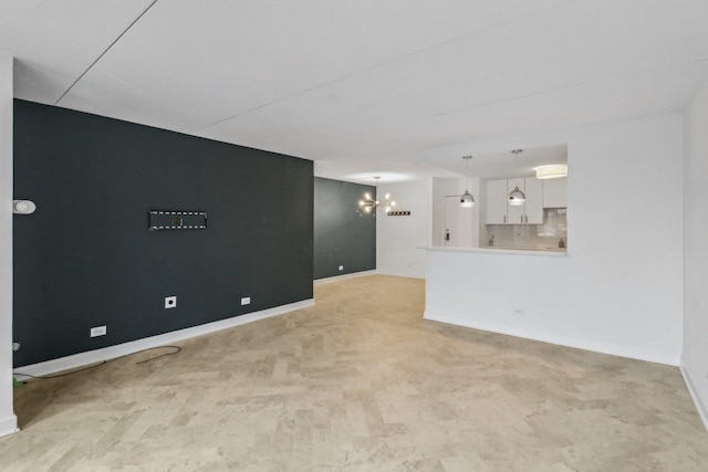 unfurnished living room featuring a chandelier and baseboards