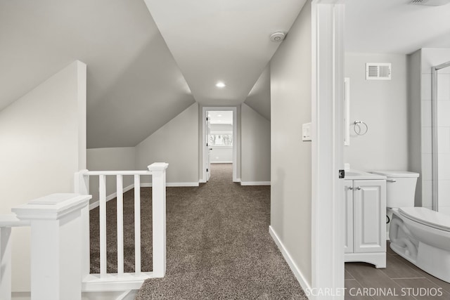 corridor with vaulted ceiling, visible vents, baseboards, and dark carpet