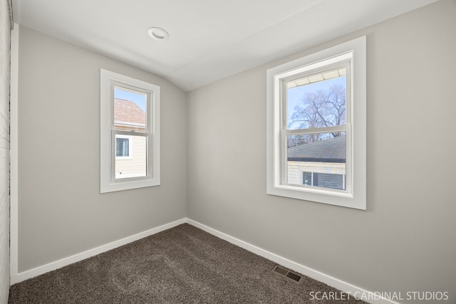 spare room featuring dark colored carpet, visible vents, and baseboards