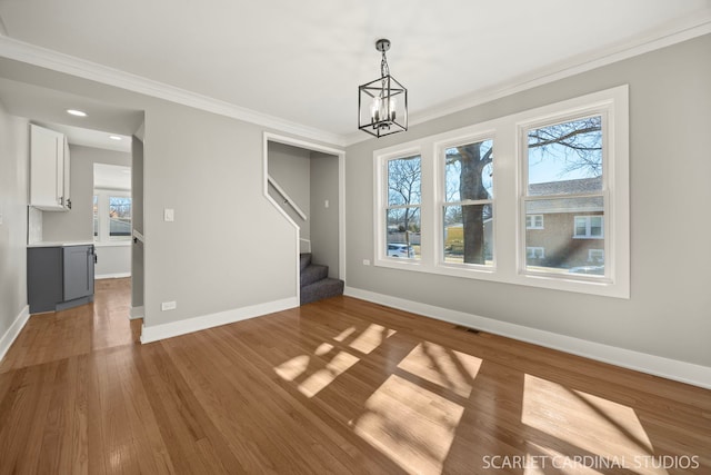 unfurnished dining area with crown molding, baseboards, stairs, wood finished floors, and a notable chandelier