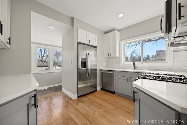 kitchen featuring a healthy amount of sunlight, gray cabinets, a sink, stainless steel appliances, and backsplash