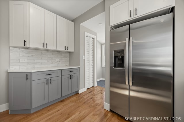 kitchen with tasteful backsplash, gray cabinetry, baseboards, light wood-style flooring, and stainless steel fridge