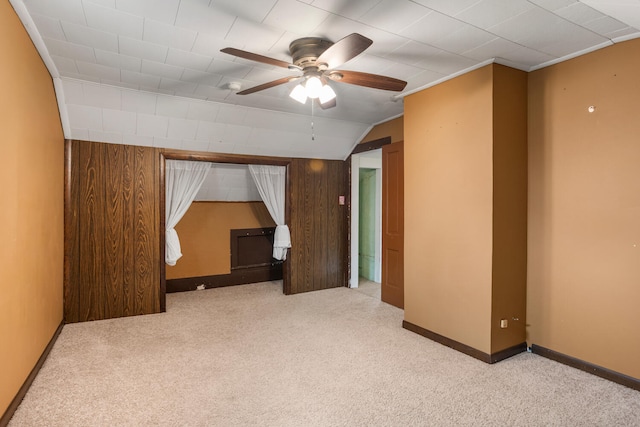 spare room with baseboards, lofted ceiling, ceiling fan, wood walls, and light colored carpet