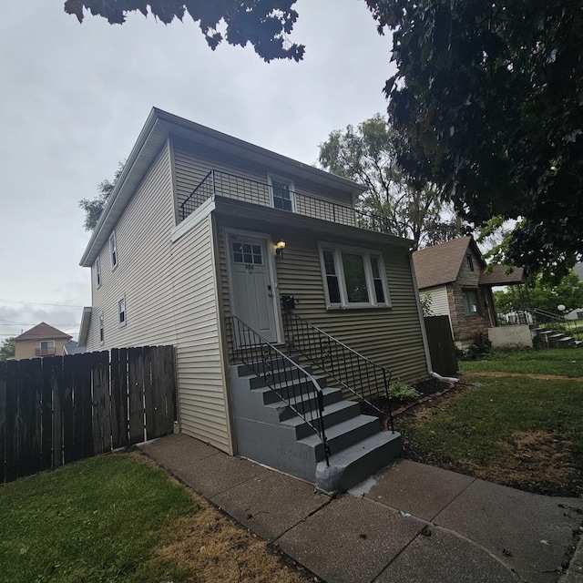 view of front facade featuring entry steps, a front lawn, fence, and a balcony