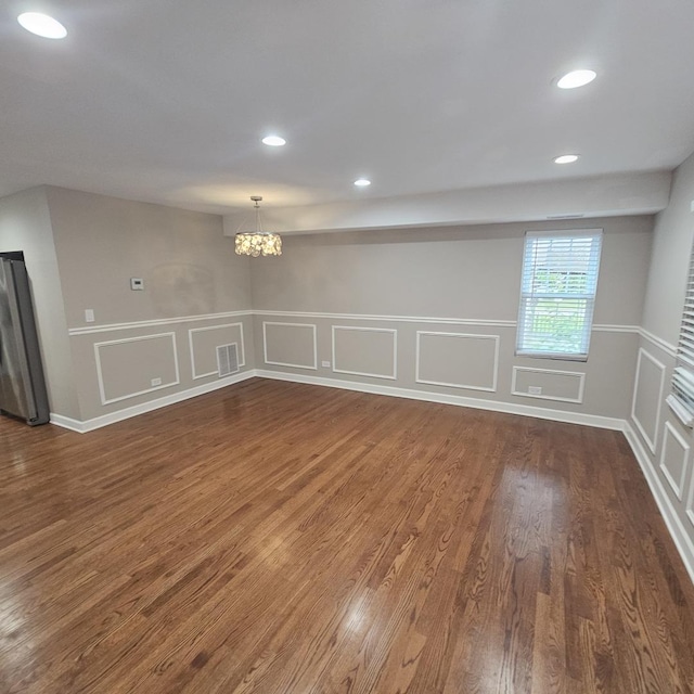 spare room featuring visible vents, dark wood-style flooring, a chandelier, a decorative wall, and recessed lighting