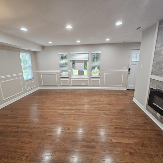 unfurnished room featuring a glass covered fireplace, dark wood-style flooring, visible vents, and a decorative wall