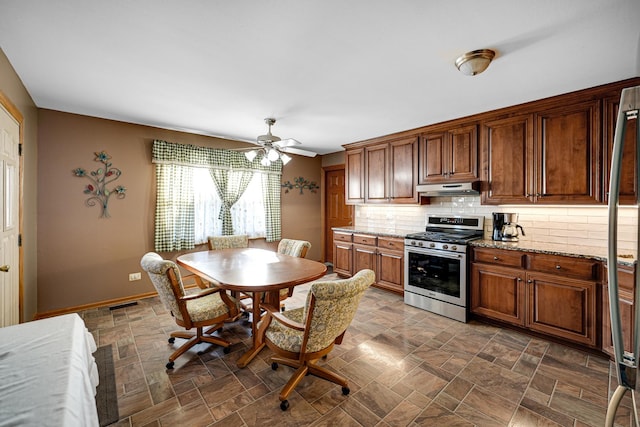 kitchen featuring tasteful backsplash, under cabinet range hood, stone finish floor, and stainless steel gas range oven