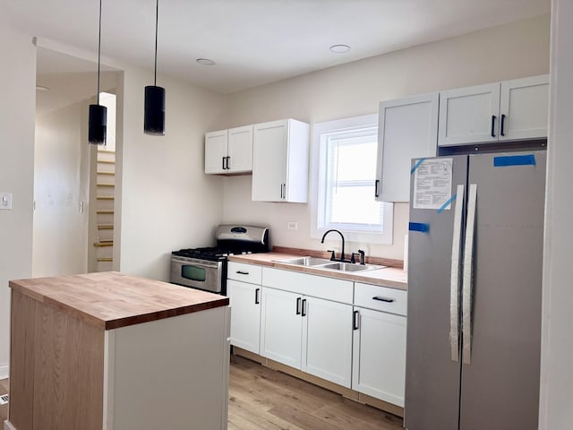 kitchen with light wood finished floors, butcher block counters, appliances with stainless steel finishes, hanging light fixtures, and a sink