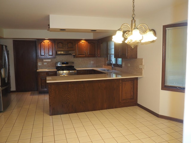 kitchen featuring a peninsula, a sink, light countertops, stainless steel gas range, and freestanding refrigerator