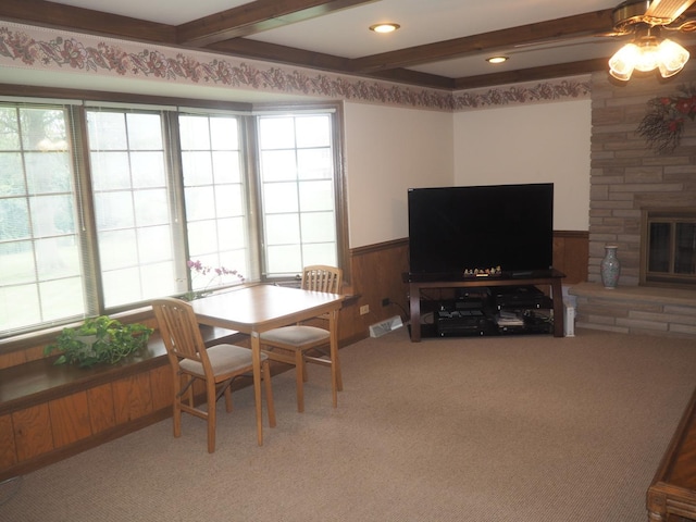 dining space featuring light carpet, a wainscoted wall, a stone fireplace, wood walls, and beam ceiling