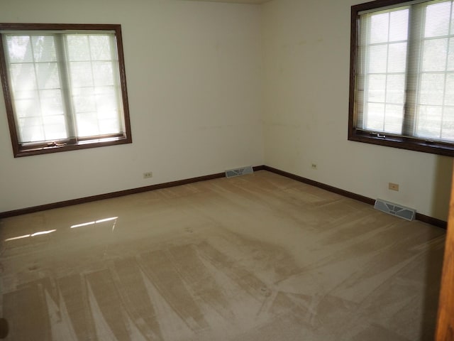 spare room with baseboards, carpet, visible vents, and a healthy amount of sunlight