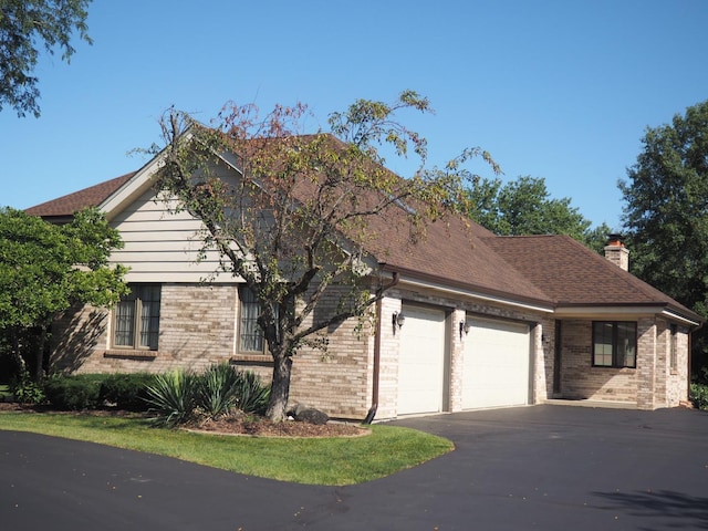 view of side of home featuring aphalt driveway, an attached garage, brick siding, a shingled roof, and a chimney