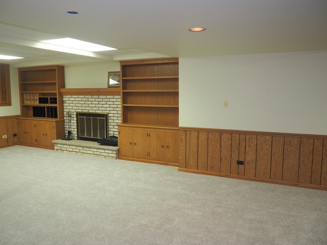 unfurnished living room with built in shelves, carpet, a brick fireplace, and a wainscoted wall