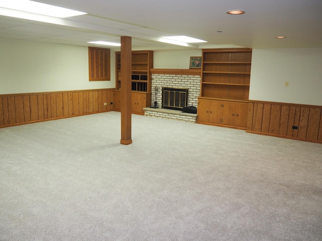 finished below grade area with carpet floors, a brick fireplace, a wainscoted wall, and wood walls