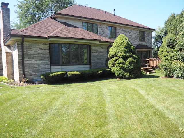 back of property with roof with shingles, a chimney, a lawn, and brick siding