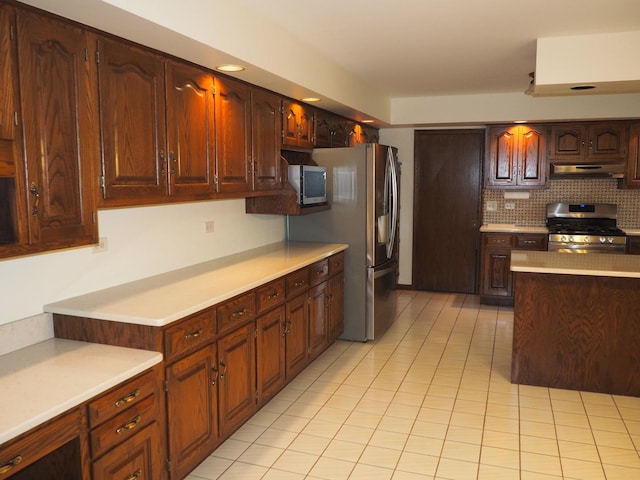 kitchen featuring light tile patterned flooring, under cabinet range hood, light countertops, appliances with stainless steel finishes, and backsplash