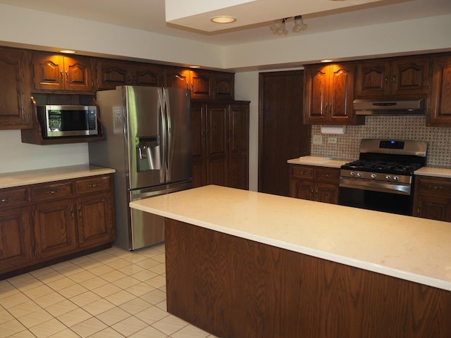 kitchen featuring light tile patterned floors, under cabinet range hood, stainless steel appliances, light countertops, and tasteful backsplash