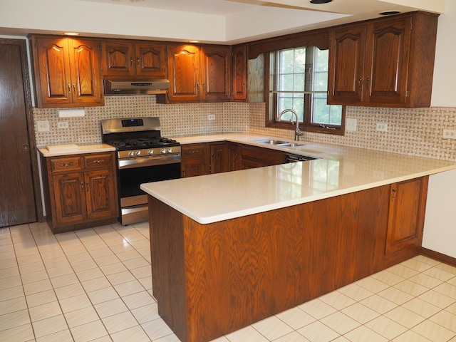 kitchen with light tile patterned floors, under cabinet range hood, a sink, light countertops, and gas stove