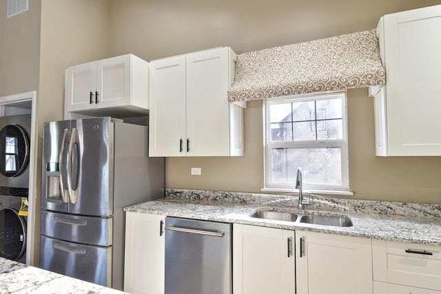 kitchen with visible vents, stacked washer and clothes dryer, white cabinets, stainless steel appliances, and a sink