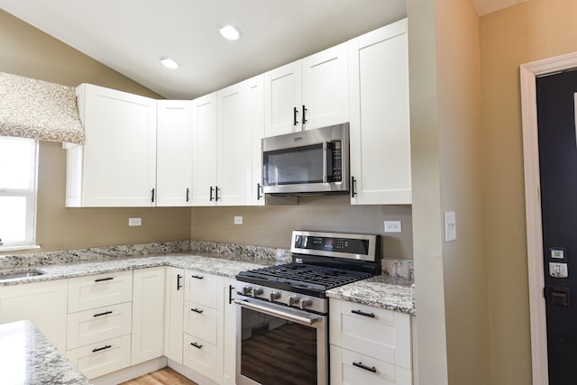 kitchen with a sink, stainless steel appliances, light stone counters, and white cabinets