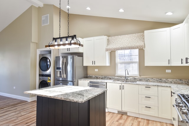 kitchen with visible vents, a sink, white cabinetry, stainless steel appliances, and stacked washer / dryer