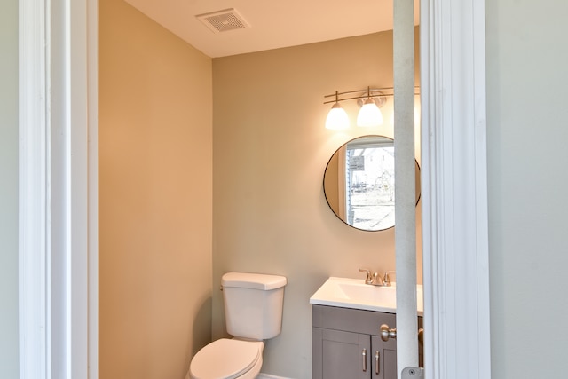 half bath featuring vanity, toilet, and visible vents