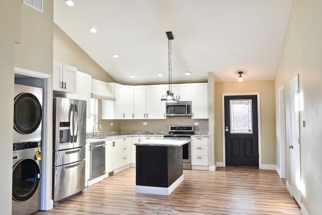 kitchen featuring a kitchen island, light stone countertops, stacked washer and dryer, stainless steel appliances, and white cabinetry